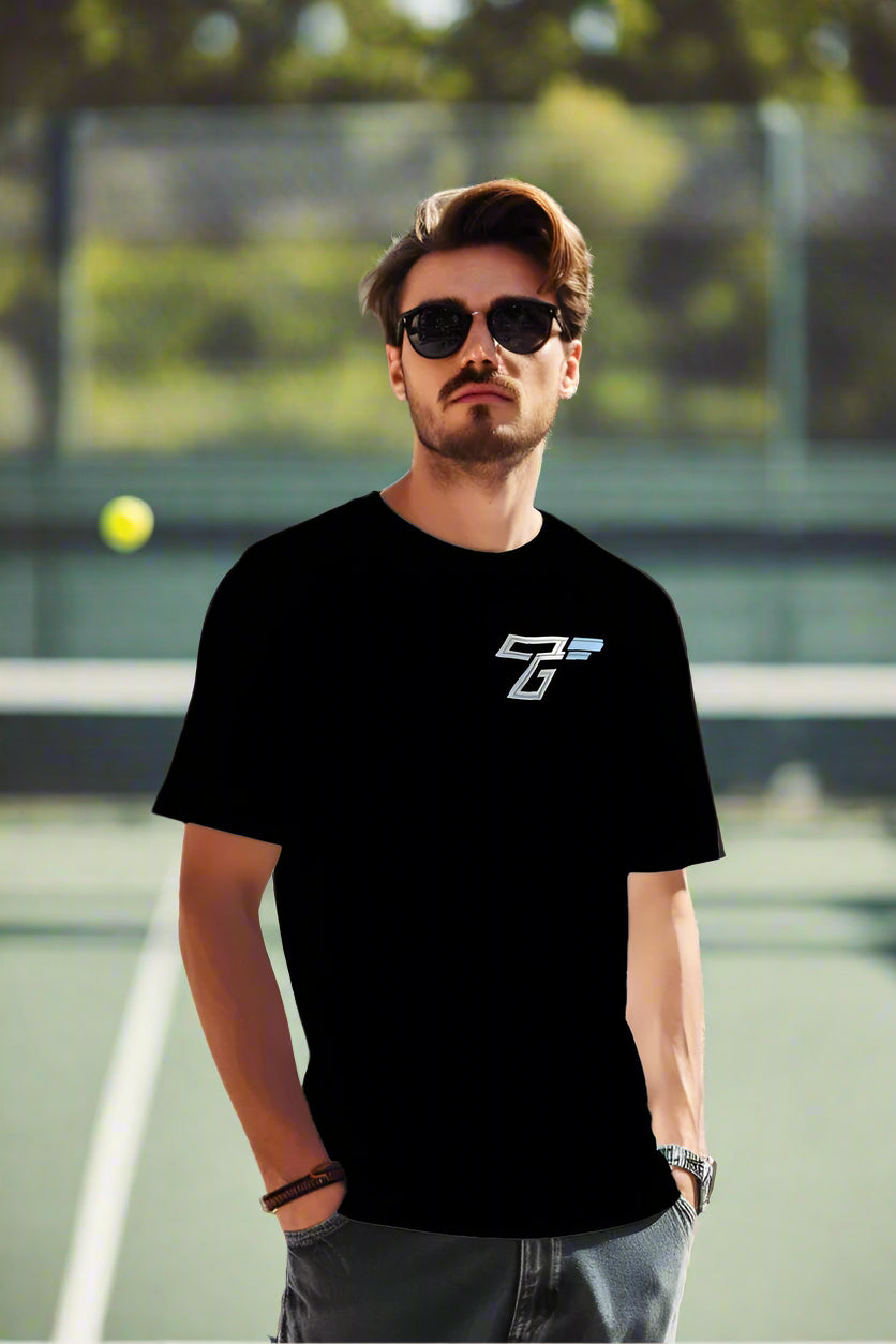 Man wearing black TriggerGrip Pro T-shirt with TG logo, standing on outdoor pickleball court in sunglasses